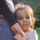 young adopted girl hugs closely to her mother's side