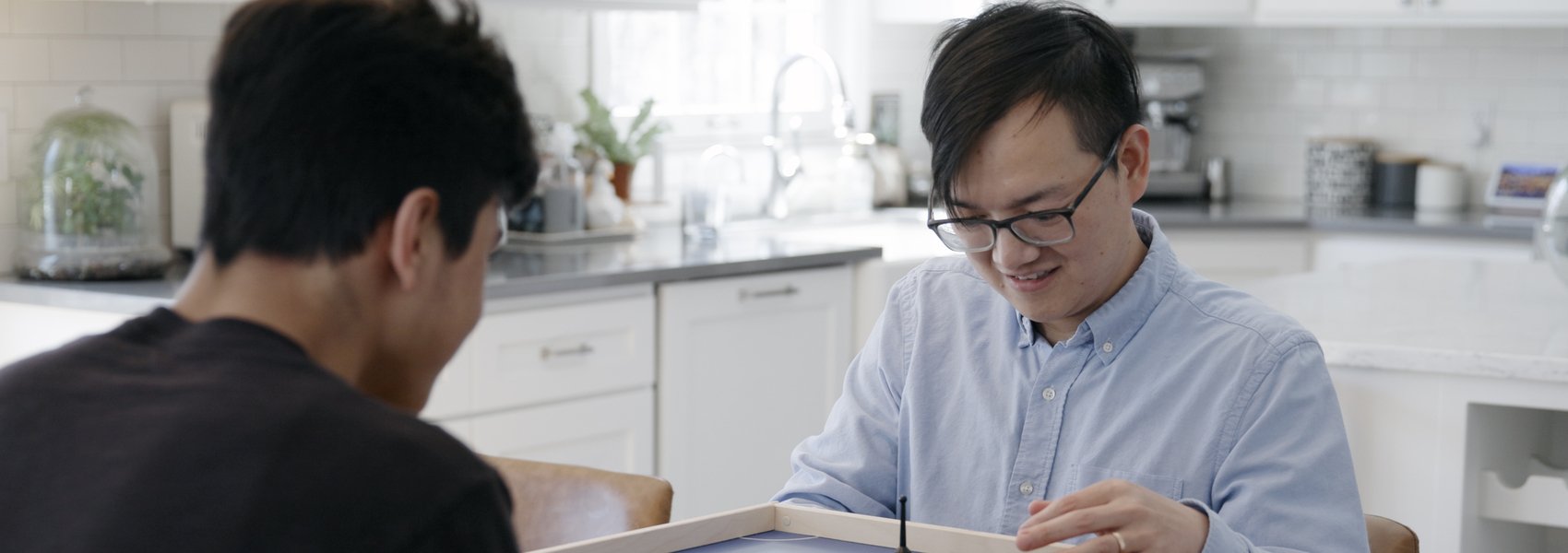 Foster dad plays a game at the kitchen table with Afghan refugee teenage boy