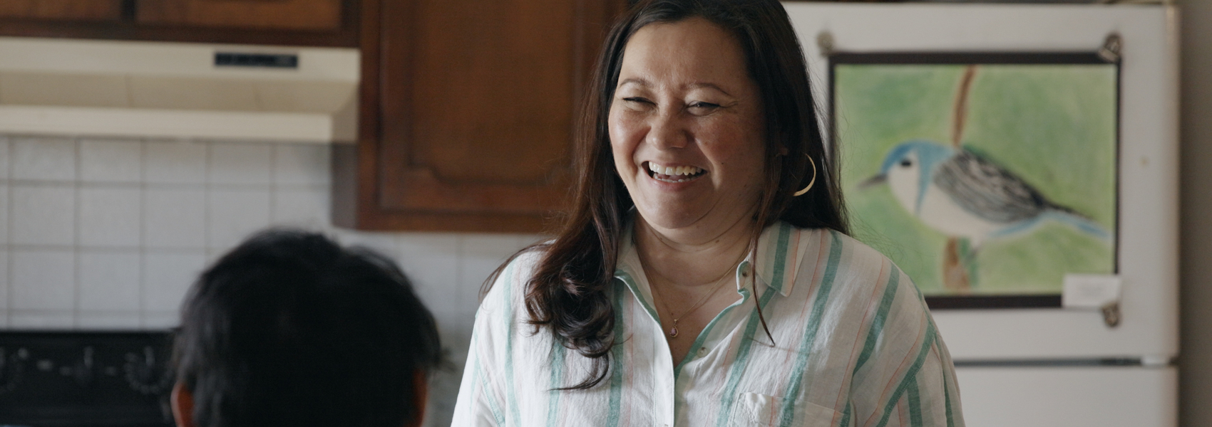 Asian foster mother talks to young refugee boy in kitchen