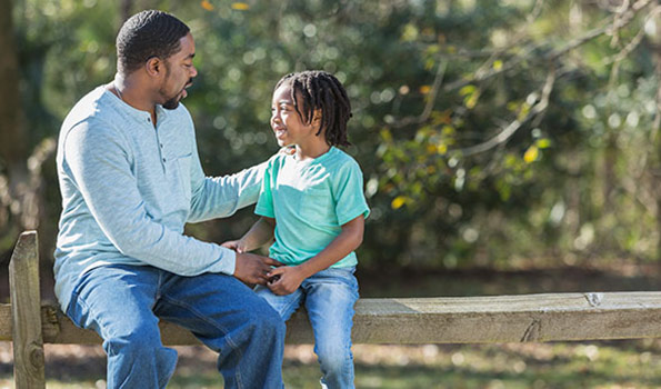 african american adoptive father speaks to his son on a park bench
