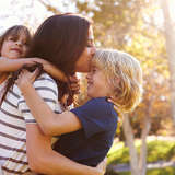 mother hugs her two young children at sunset