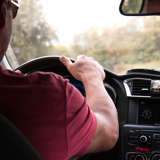 white man holds the wheel of his car while driving