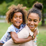 african american birth mother holds her daughter on her back during an open adoption visit