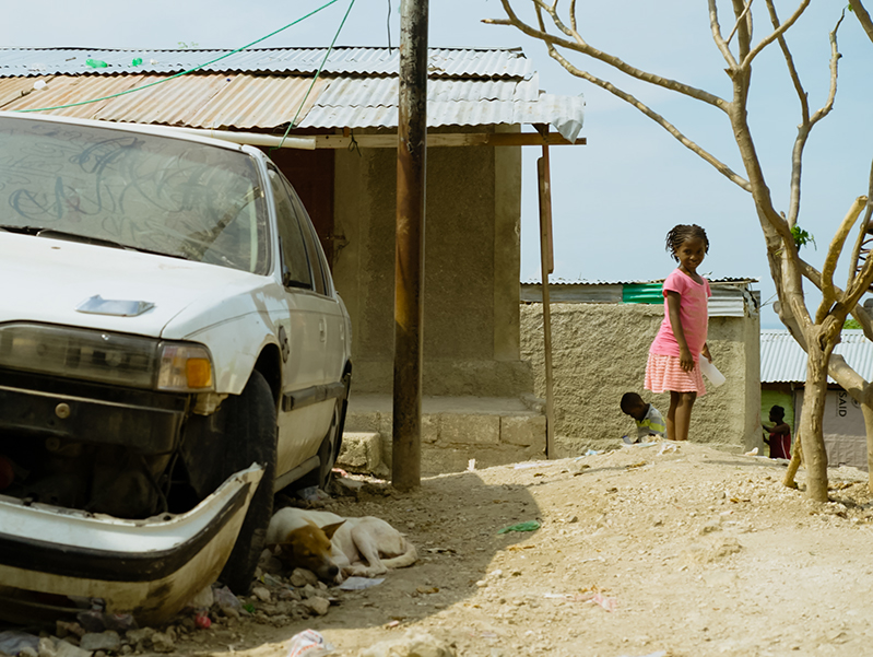 young Haitian girl looks at the wreckage of a car after the hurricane