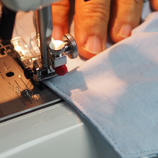 A man's hand using a sewing machine to make masks